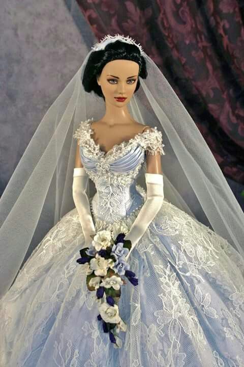 a doll dressed in a wedding dress and veil with flowers on the bottom of it