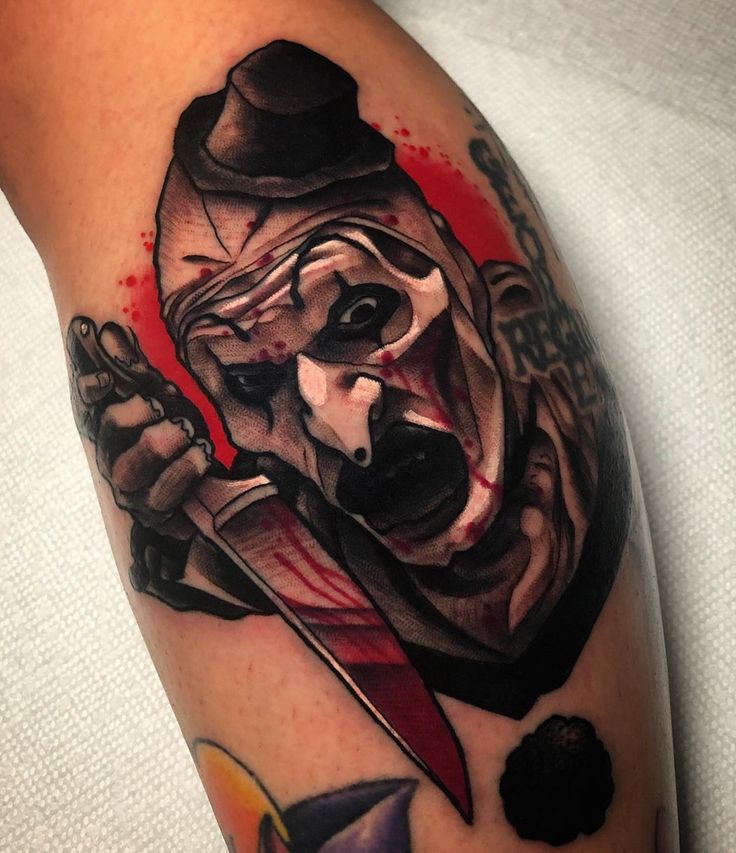 a man's arm with a tattoo of a clown holding a knife and wearing a top hat