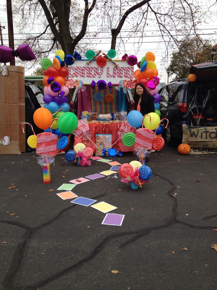 a carnival float with balloons and streamers on the ground in front of a car