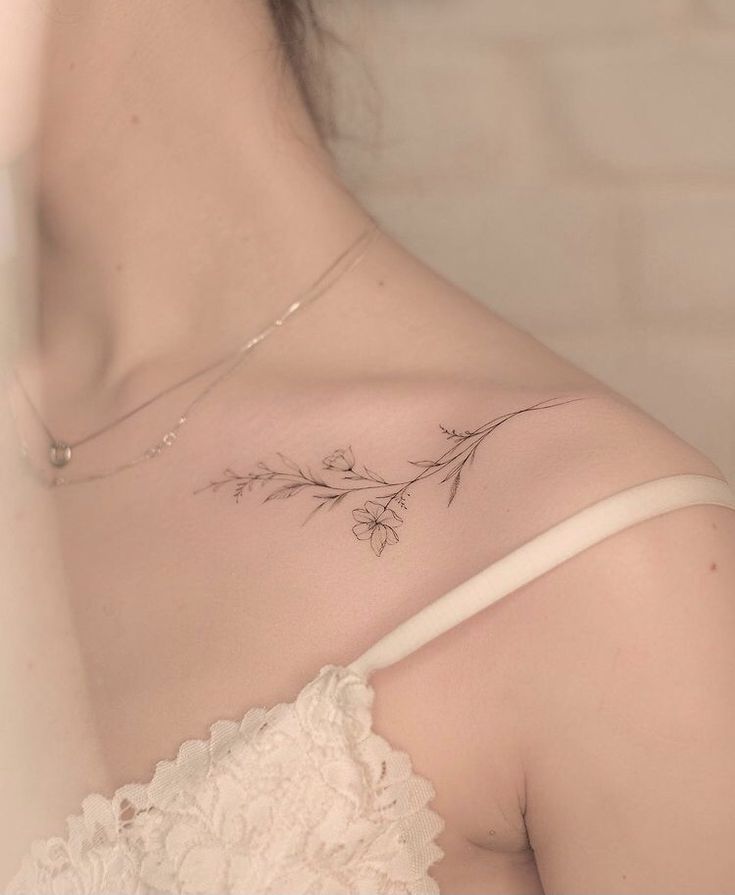 the back of a woman's shoulder with flowers tattooed on her left arm and chest