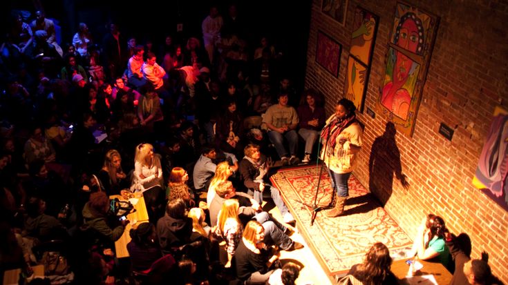 a woman standing on top of a bed next to a crowd of people in a dark room