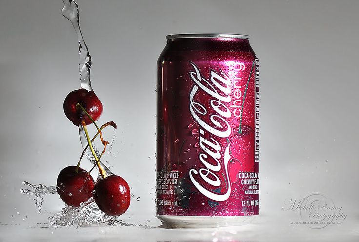 a can of coca - cola with some cherries falling out of it and water splashing on the side