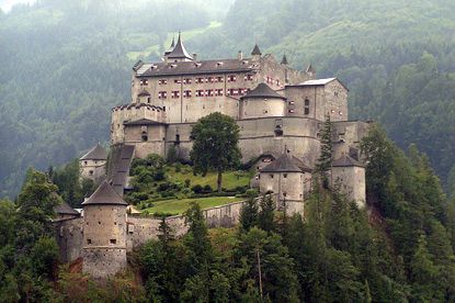 an old castle sitting on top of a hill surrounded by trees and hills in the background