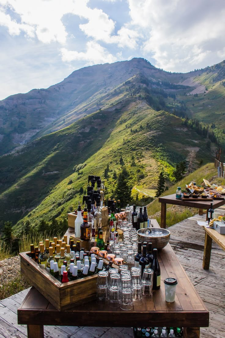 a table with bottles and glasses on top of it in front of a mountain range