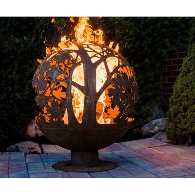 a fire pit sitting on top of a brick patio next to trees and bushes in the background