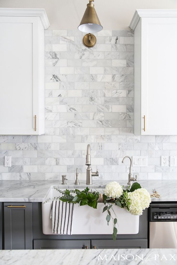 a white kitchen with marble backsplash and gold faucet light over the sink