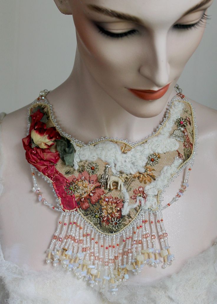 "This one-of-a-kind, fantasy bib necklace is a sweetheart with its \"Mary Had a Little Lamb\" nursery rhyme theme!       Red silk tufted fabric adorns its antique tapestry base. Authentic felted lamb's wool, metal flowers, vintage hat posy, and antique lamb add uniqueness. Additional silver charms and shiny, faceted pink glass beads enrich its splendor. All is stunningly surrounded by myriad white and beige Czech glass seed beads above its rich, glass fringe.     Vintage gold white clear chain makes this beauty fully adjustable to approximately 22\"; all is carefully backed with soft, tan Ultra Suede.       This unique neck piece will definitely prove a conversation starter when worn. It's fun and whimsical." Whimsical Handmade Necklaces For Weddings, Unique White Necklaces For Crafting, Handmade Bohemian Bridal Pendant Necklace, Whimsical White Wedding Necklaces, Wearable Art Beaded Necklace As A Gift, Beaded Necklaces As Wearable Art Gifts, Beaded Necklace As Wearable Art Gift, Beaded Necklaces As Wearable Art For Gifts, Whimsical One-of-a-kind Necklace As A Gift