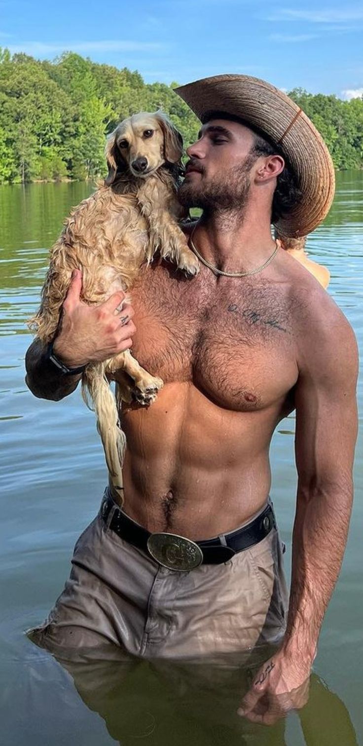 a shirtless man holding a dog in the water