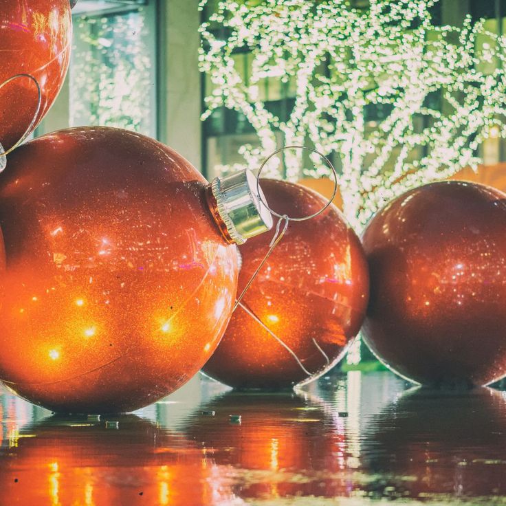 three shiny red ornaments sitting on top of a table next to a tree with lights