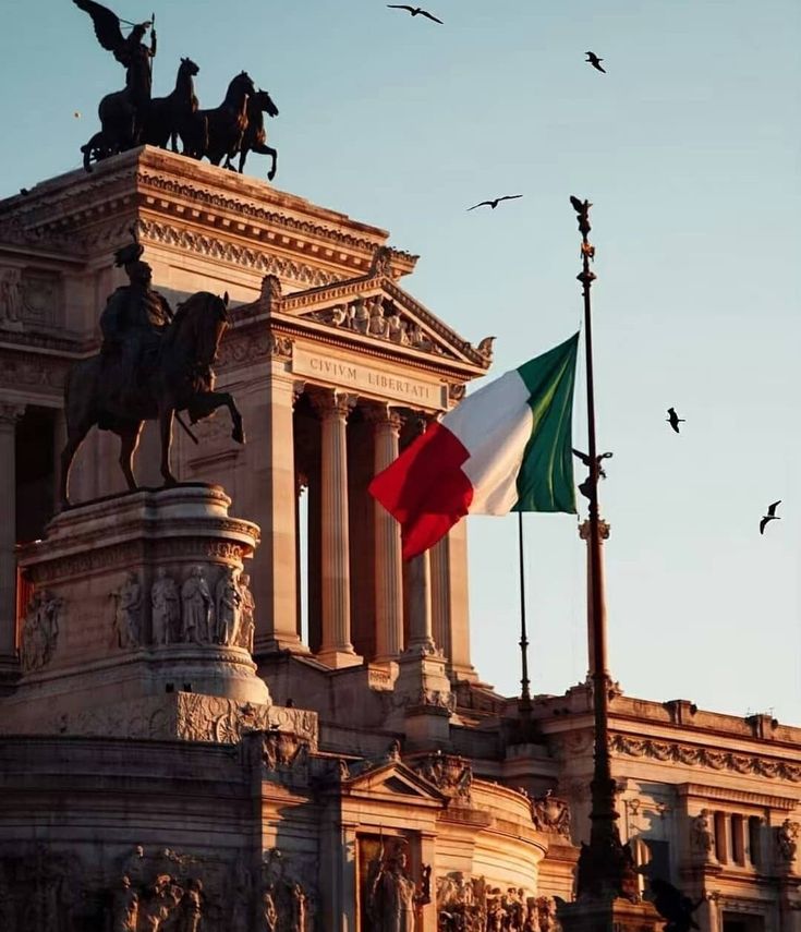 an italian flag flying in front of a building with statues on it's sides