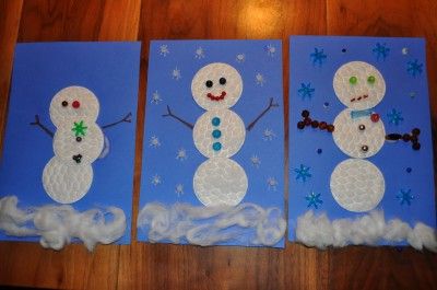 three snowmen made out of paper sitting on top of a wooden table