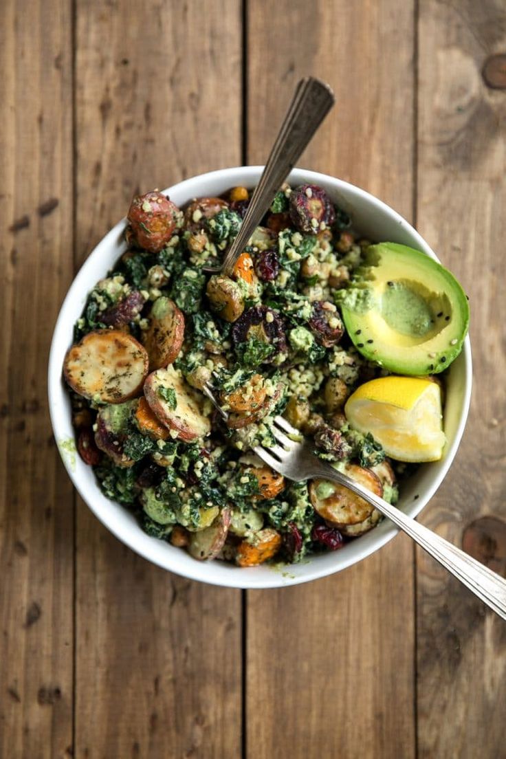 a white bowl filled with vegetables on top of a wooden table next to a fork