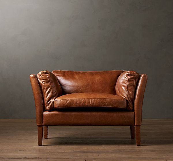 a brown leather chair sitting on top of a wooden floor next to a gray wall