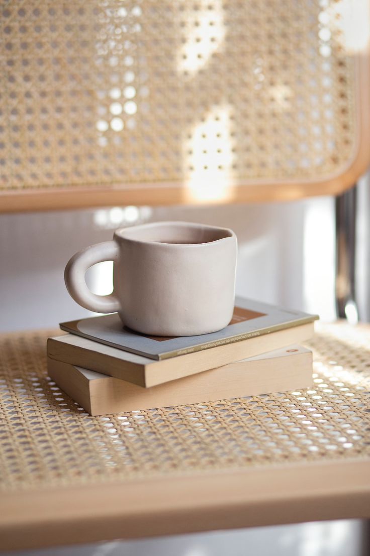 a white cup sitting on top of a stack of books next to a wooden bench