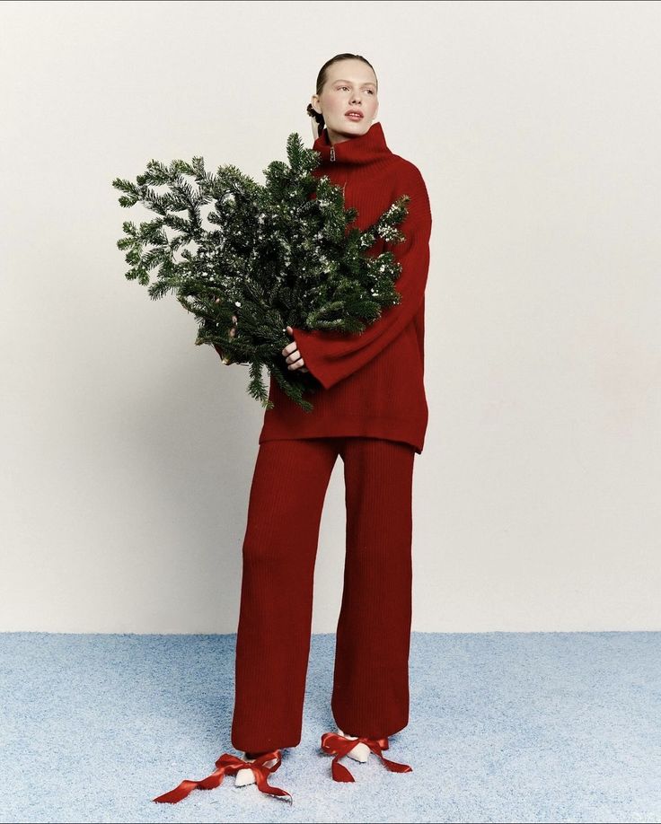 a woman in red is holding a christmas tree