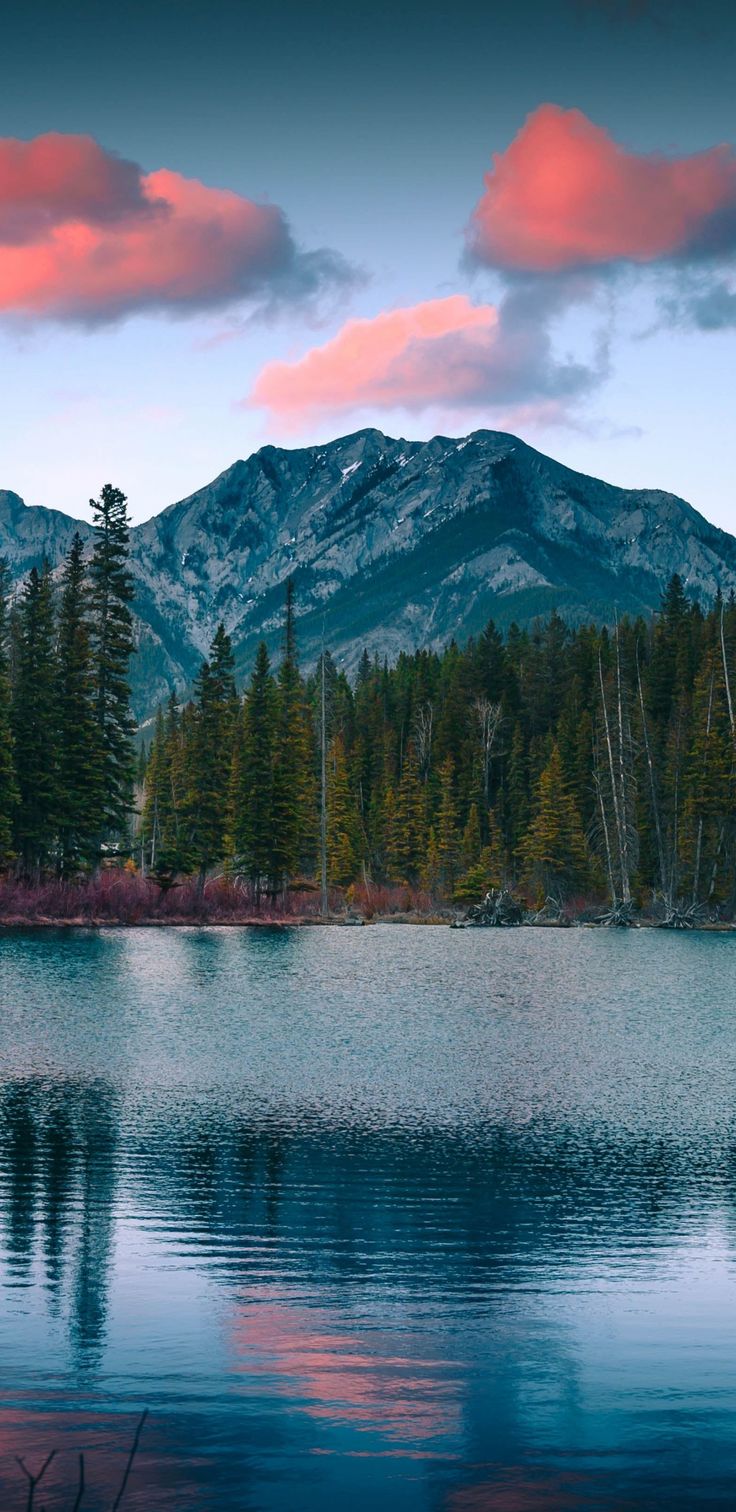 a lake with mountains in the background and trees on both sides at sunset or sunrise