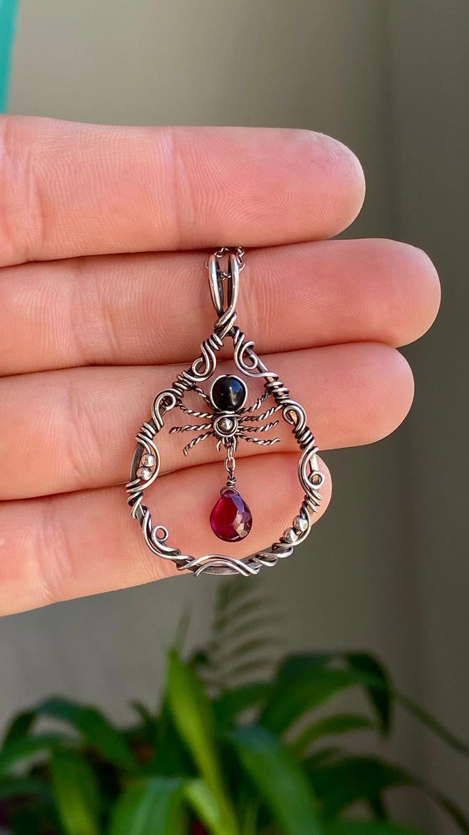 a person is holding up a pendant with a red and black stone in the center