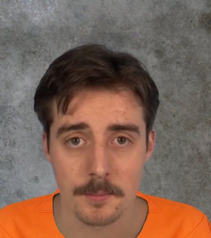 a man in an orange shirt is looking at the camera with a moustache on his face