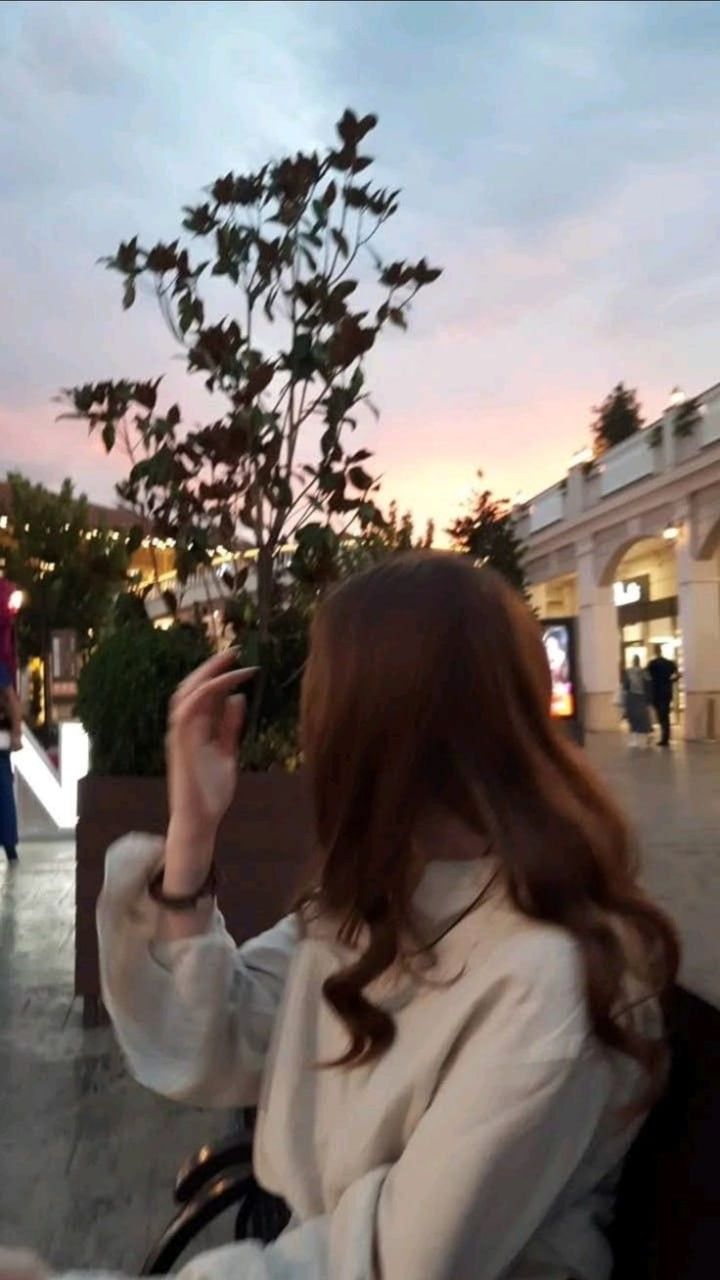 a woman is sitting on a bench and looking at her cell phone in the air