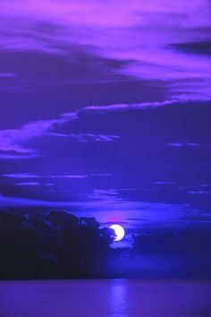 the moon is shining brightly in the sky above the water at night with purple hues