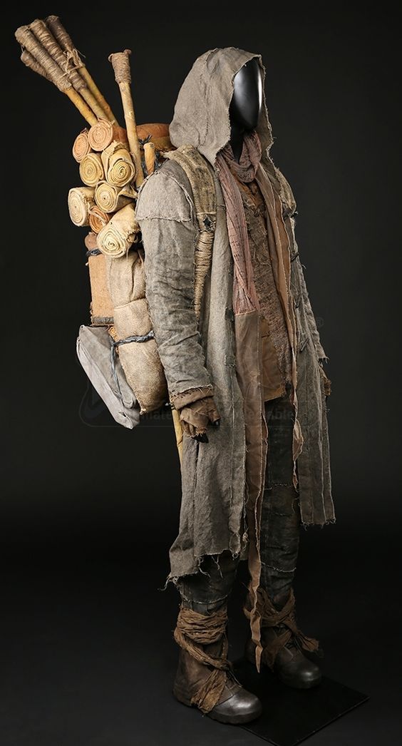 a man in a gas mask and jacket with wood logs on his back, standing against a black background