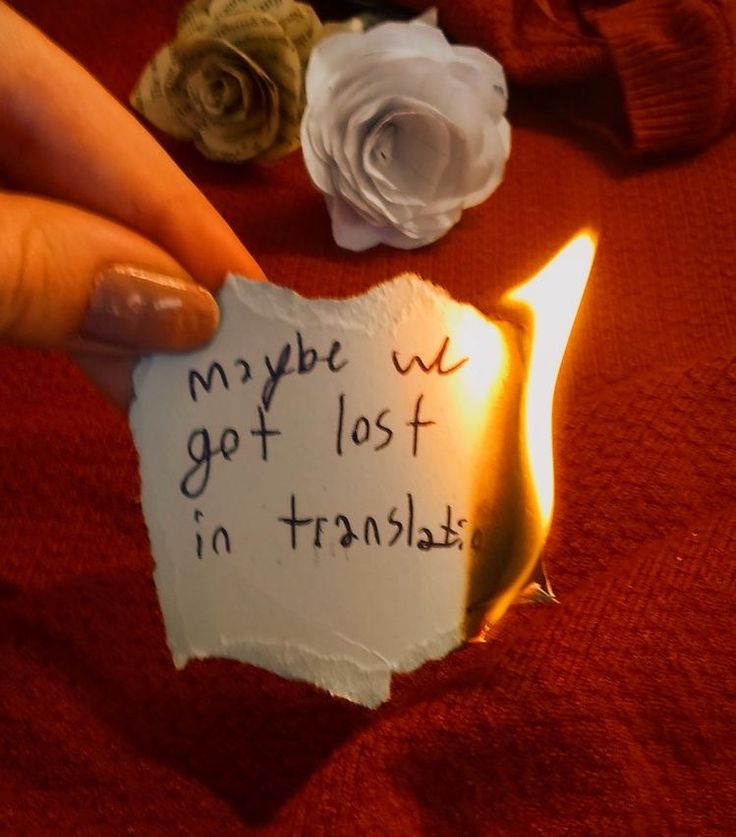 someone holding up a piece of paper with writing on it next to flowers and a candle