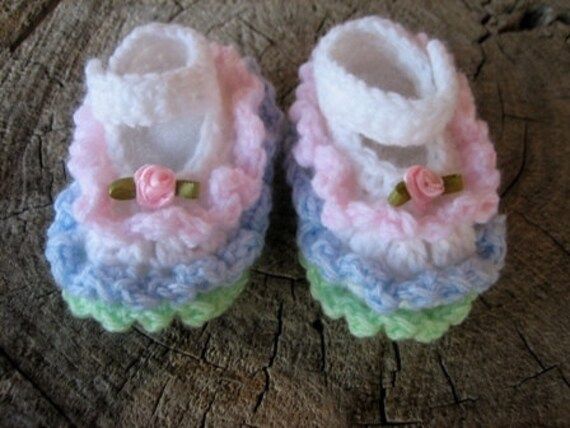 small crocheted baby booties with bows on the front and bottom, sitting on a piece of wood