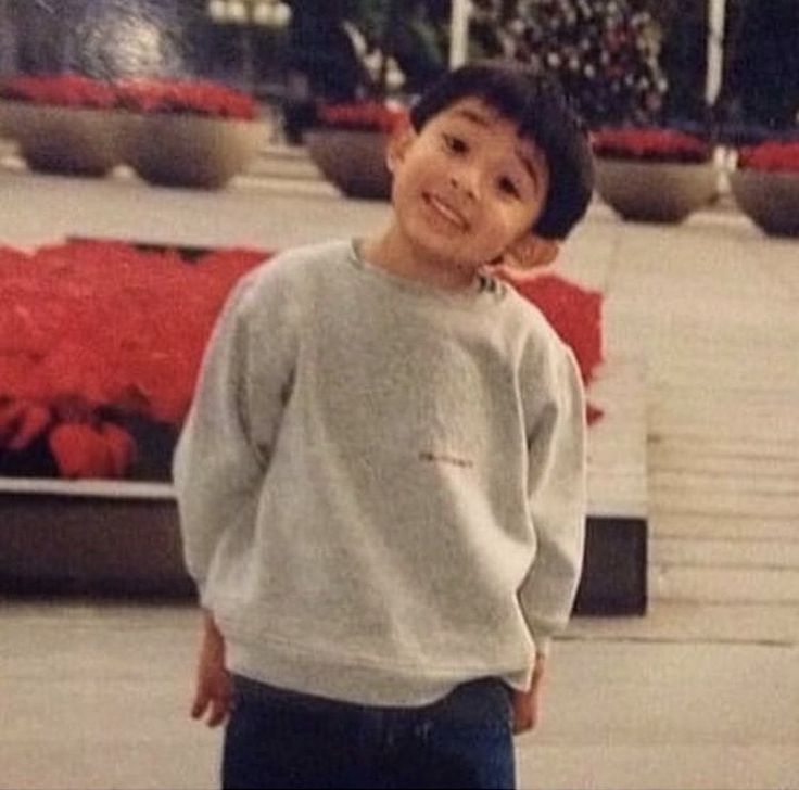 a young boy is standing in front of some red flowers and looking at the camera