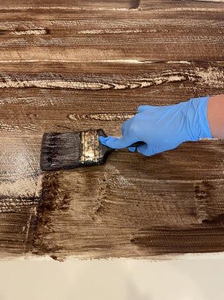 a person in blue gloves is using a brush to paint the top of a piece of wood