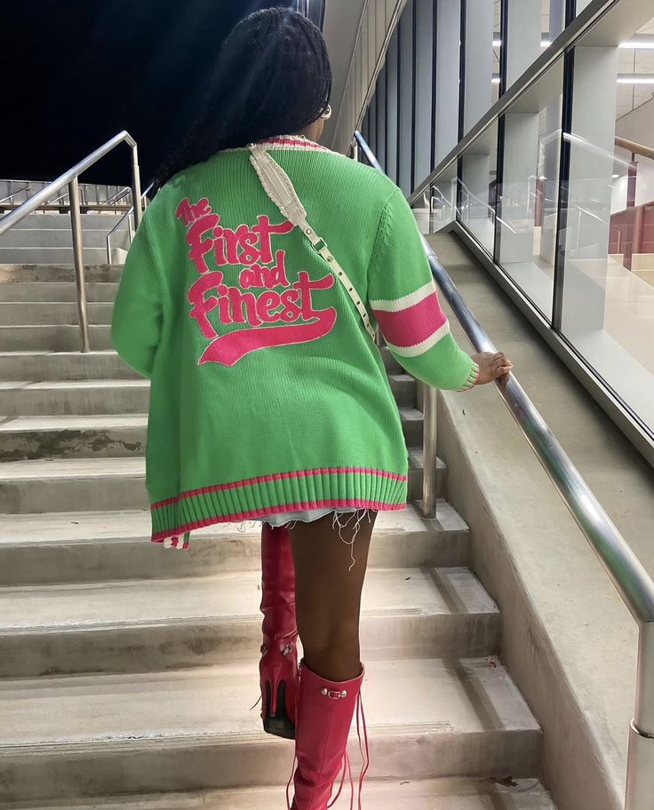 a woman is walking down the stairs with her pink boots and green sweater over her shoulders