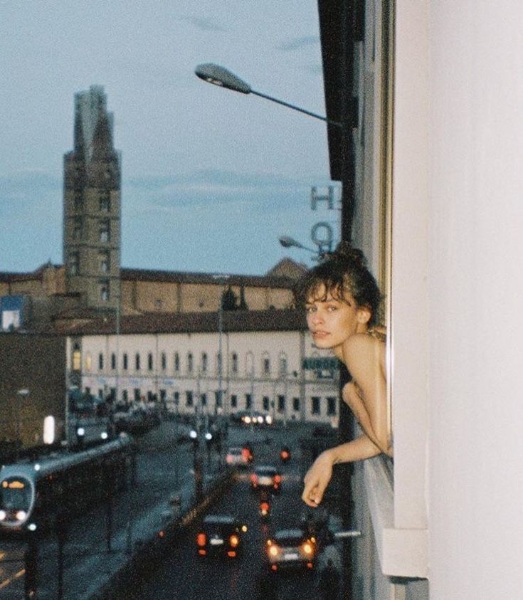 a young man standing on the ledge of a window looking out at a city street