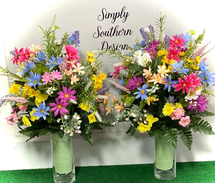 two vases filled with colorful flowers sitting on top of a green carpeted floor