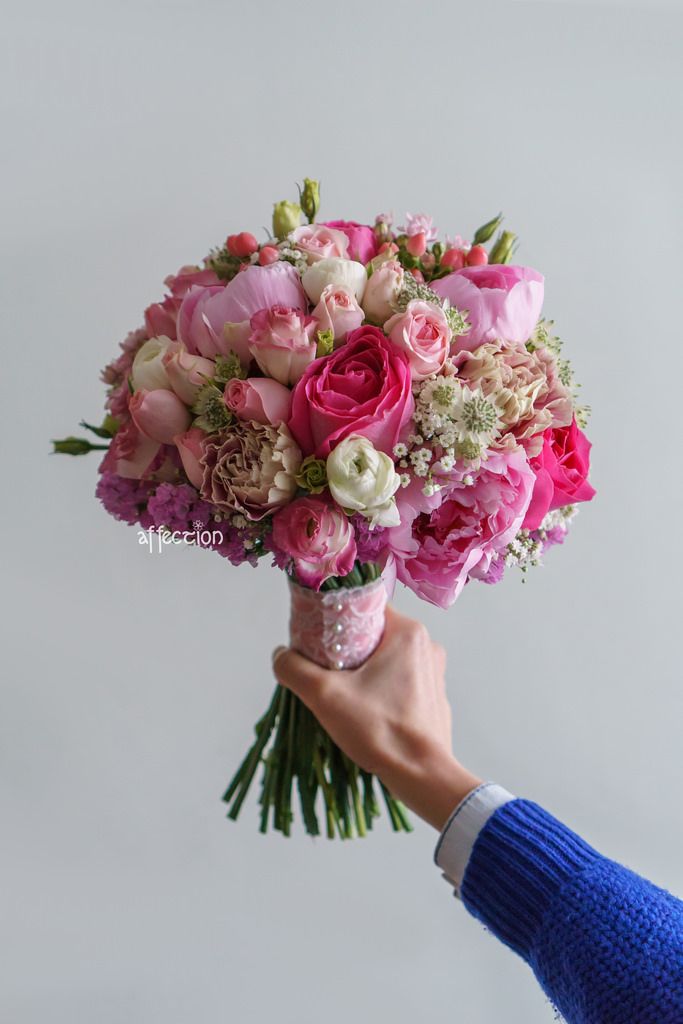 a person holding a bouquet of pink and white flowers in their left hand, with the other hand reaching for it