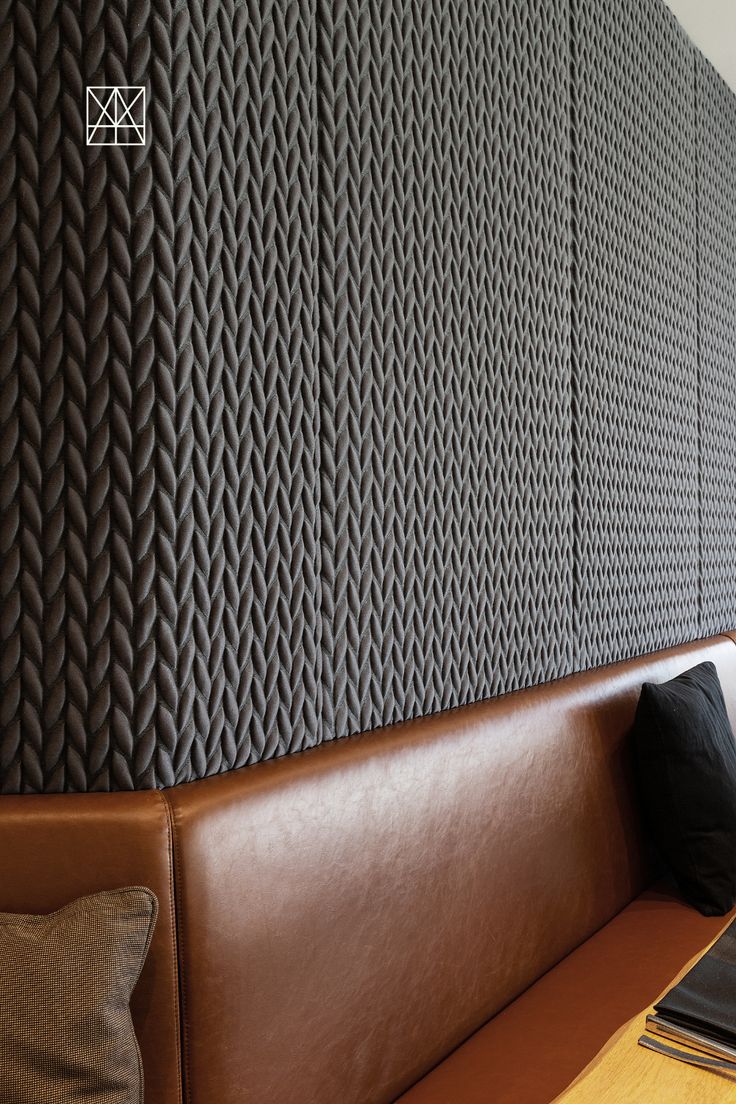 a brown leather bench sitting in front of a wall covered with knitted panels and pillows