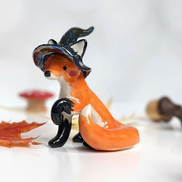 a figurine of a fox wearing a witches hat sitting on top of leaves