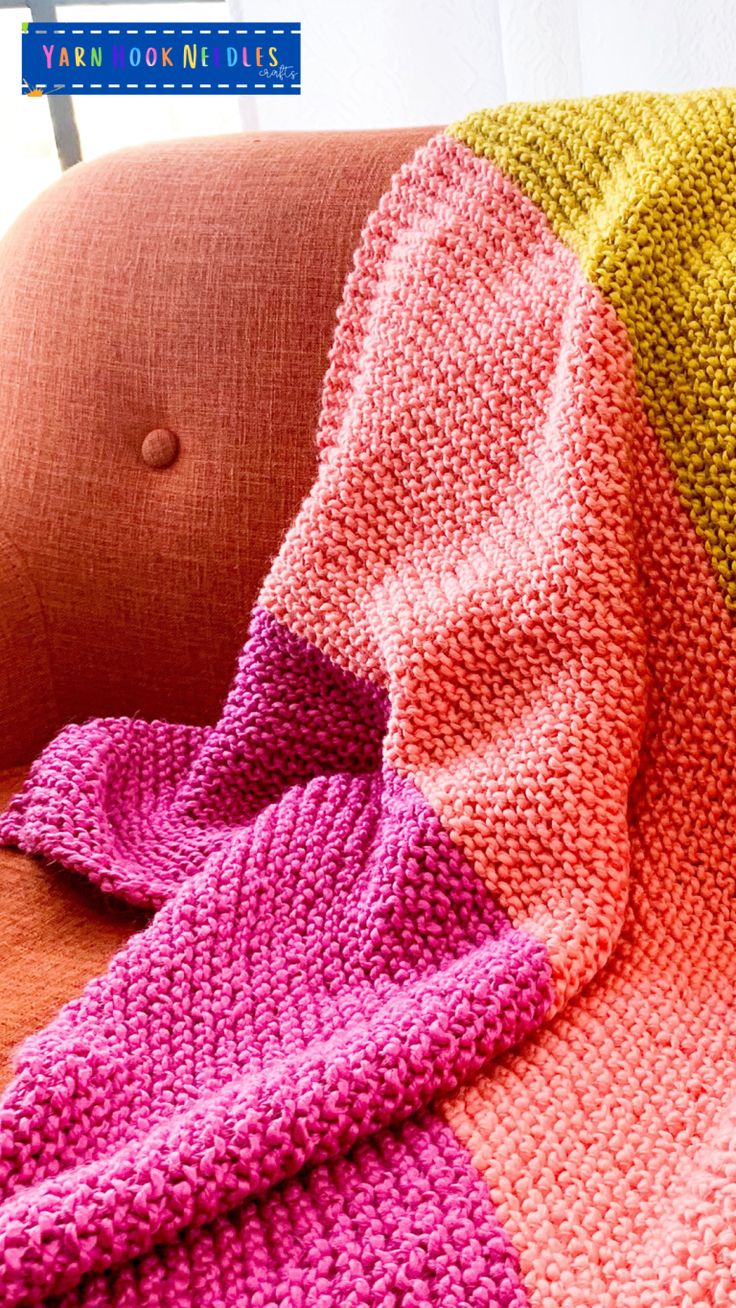 a knitted blanket sitting on top of a couch next to a pink and yellow pillow