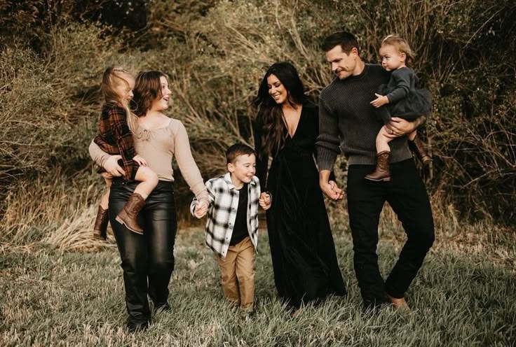 a group of people holding hands and walking through the grass with one child in his arms