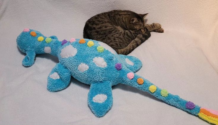 a cat laying on top of a bed next to a blue stuffed animal with multicolored spots