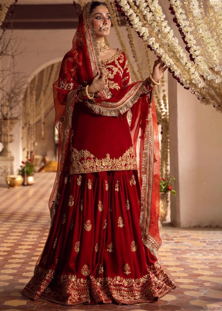 a woman in a red and gold bridal gown standing under an arch with flowers