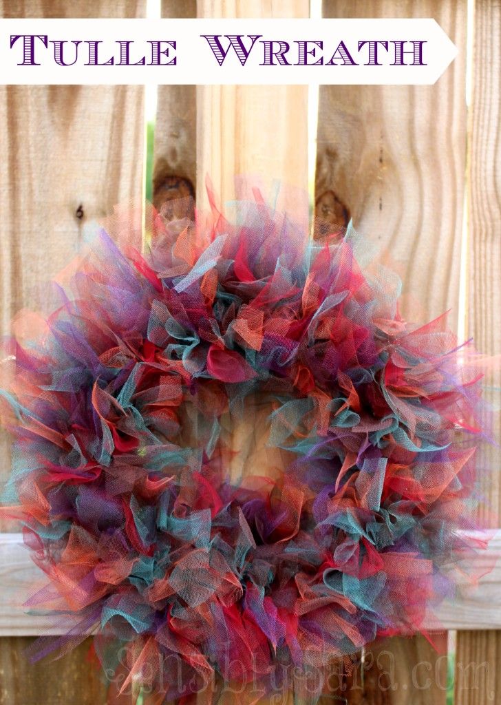 a colorful wreath hanging on the side of a wooden fence with text overlay that says tulle wreath