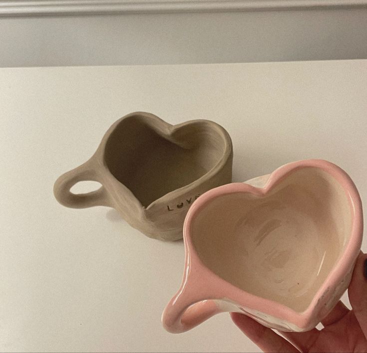 two ceramic heart shaped mugs sitting on top of a white table next to each other