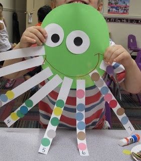 a young boy holding up a paper cut out of an octopus's head with colored dots