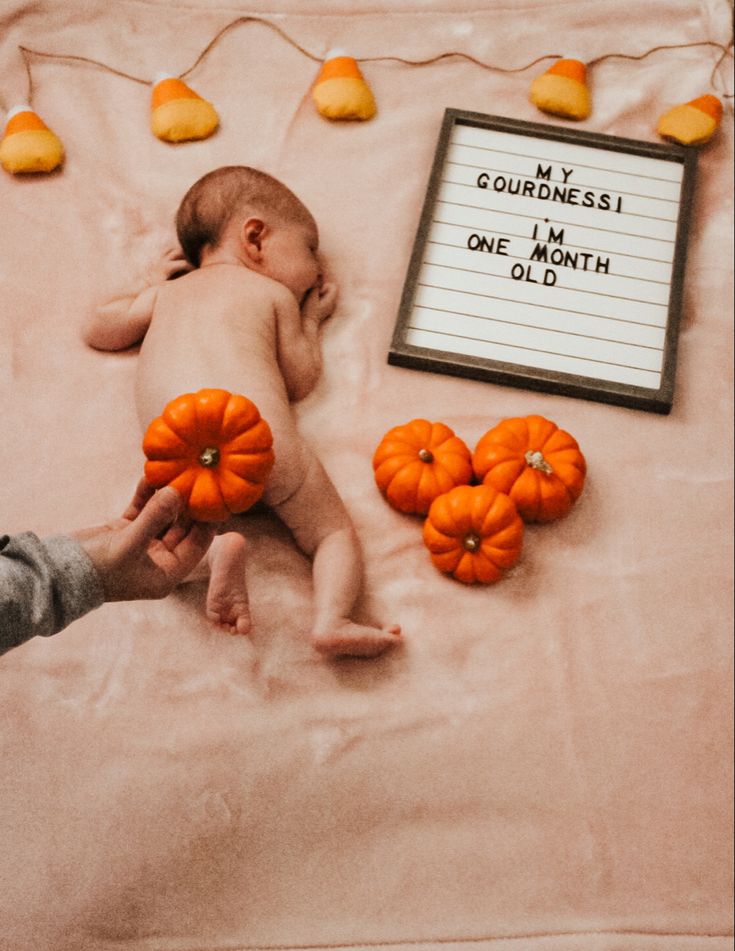 a baby laying on top of a bed next to pumpkins and a sign that says gourdress i'm one month old