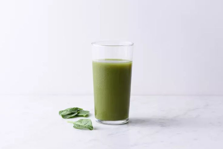 a glass filled with green liquid next to leaves