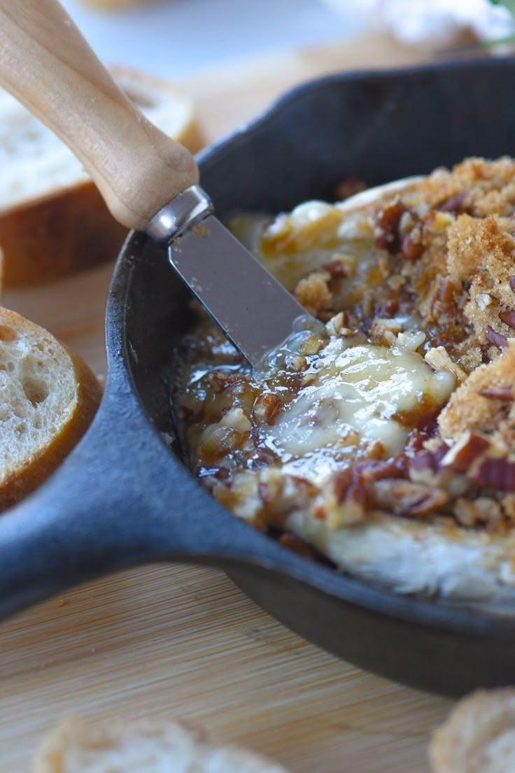 a skillet filled with food sitting on top of a wooden table next to bread