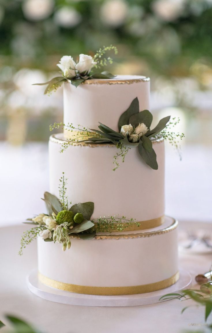 a three tiered white cake with greenery on top