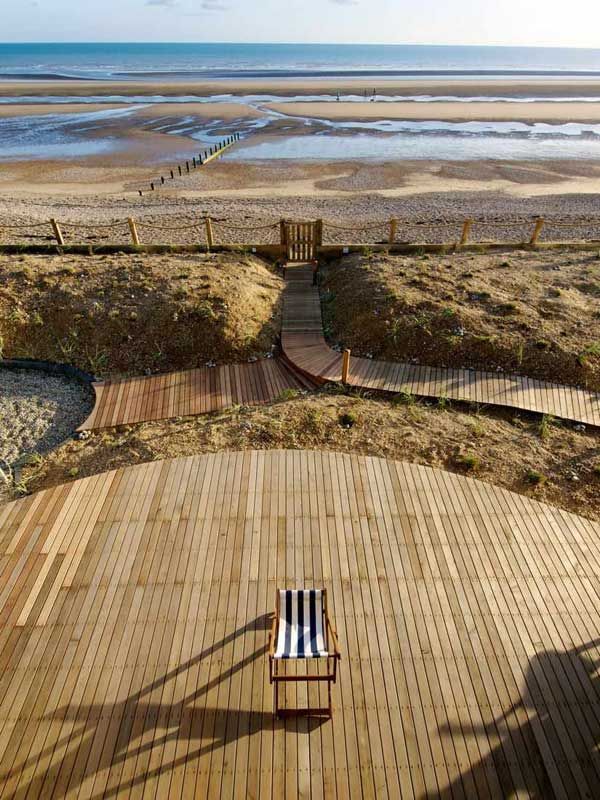 a chair sitting on top of a wooden deck next to the ocean in front of a sandy beach