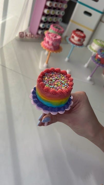 a hand holding a cake with sprinkles on it in front of other cakes