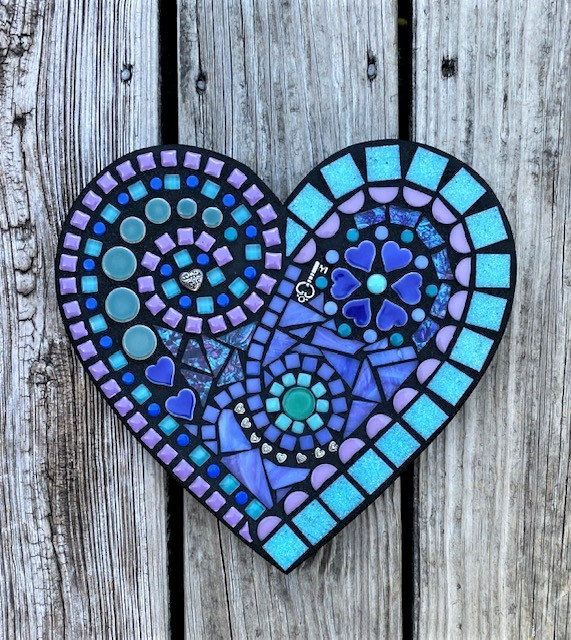 a heart shaped stained glass decoration on a wooden fence with blue and purple designs in the center