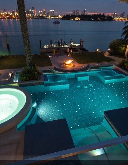 an outdoor swimming pool at night with lights on the water and palm trees in the background